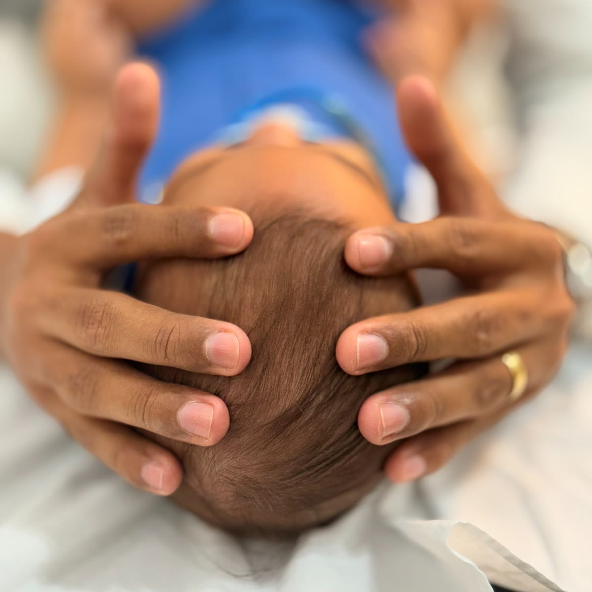 Mãos do Dr. Hidelvani aplicando técnica craniana suave na cabeça de um bebê